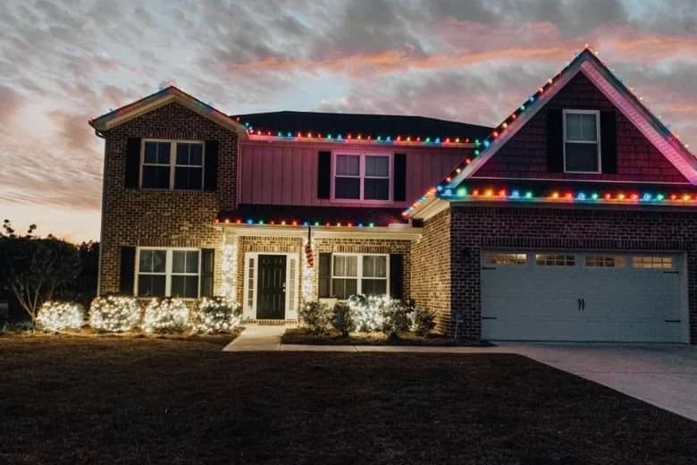 A brick home with multicolored Christmas roofline lights at sunset