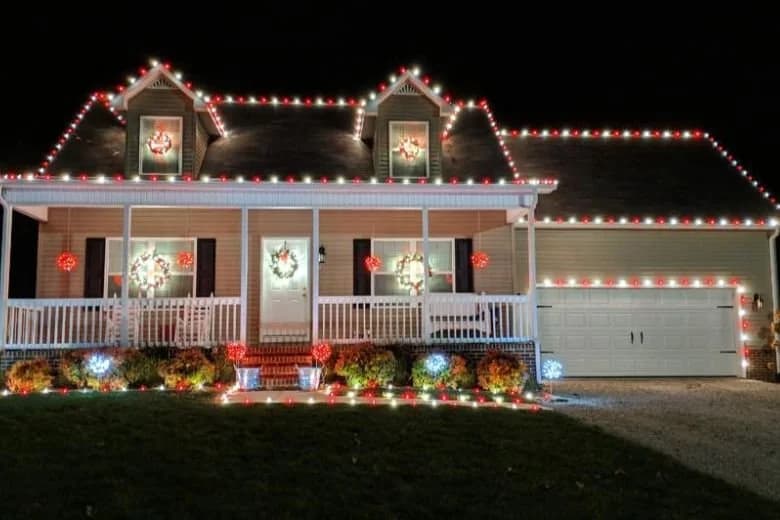 Red and white Christmas lights decorating a home’s roofline and front porch